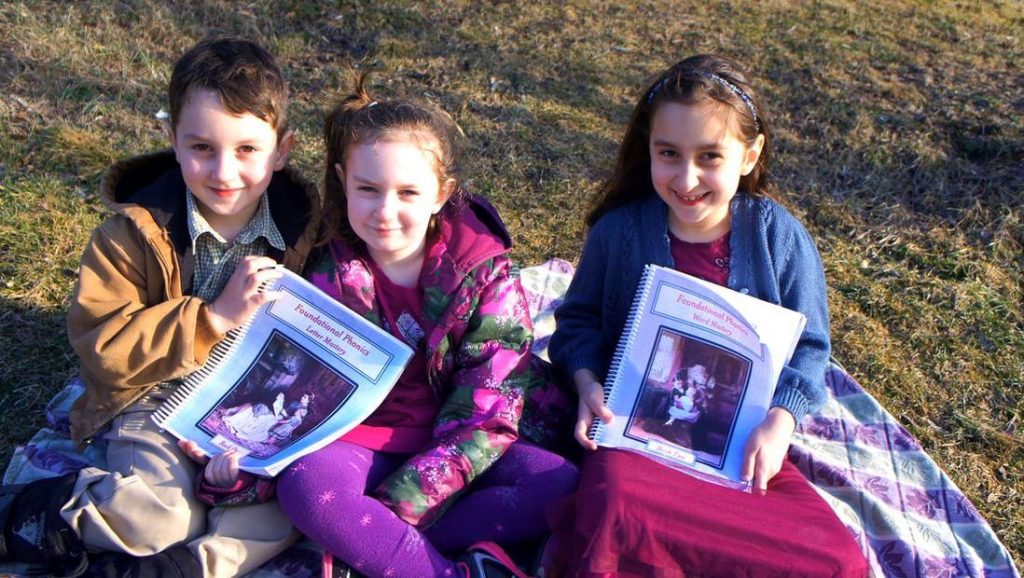Three children holding Foundational Phonics curriculum